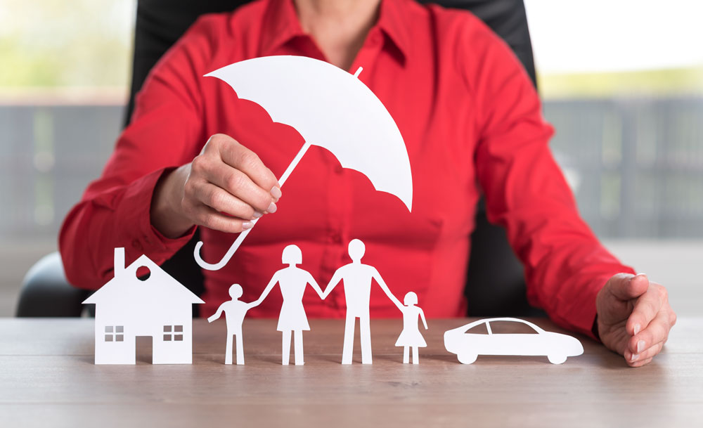 insurance provider holding a umbrella over paper cutouts of a house family and car