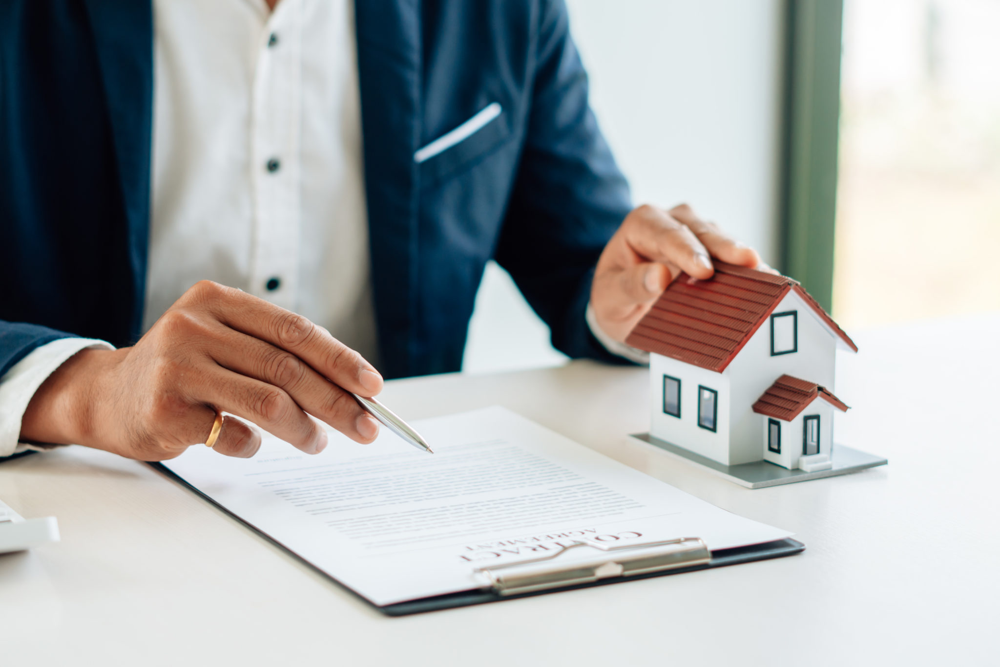 Man with hand on a small model home reviewing a home insurance policy